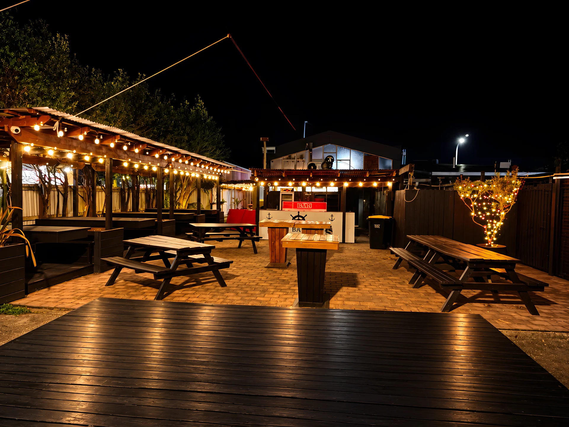 Shipwreck Bar garden bar at night, with picnic tables, a timber deck and festoon lights over the covered seating